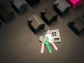 A set of keys rests on a surface surrounded by small black 3D-printed house models, symbolizing homeownership and real estate.