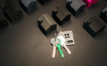 A set of keys rests on a surface surrounded by small black 3D-printed house models, symbolizing homeownership and real estate.