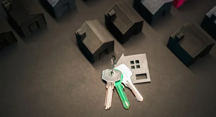 A set of keys rests on a surface surrounded by small black 3D-printed house models, symbolizing homeownership and real estate.