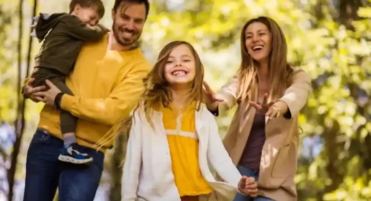 A joyful family enjoys a day outdoors, with two adults and two children playing among vibrant greenery in the background.