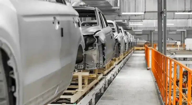 A row of unfinished car bodies on an automated assembly line within a modern factory setting, showcasing an industrial production scene.