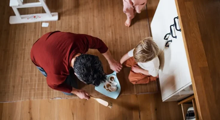 A parent serves snacks to a child seated on the floor, while another child watches nearby in a cozy home setting.