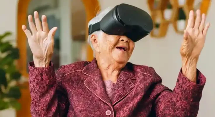 An elderly woman wearing a virtual reality headset, smiling and gesturing with her hands, seated in a cozy living room setting.