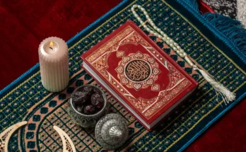 A beautifully ornate Quran rests on a colorful prayer mat alongside a lit candle, dates, and prayer beads, evoking a serene atmosphere.