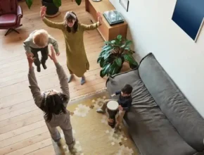 A lively indoor scene with children playing; one child is lifted in the air, while another plays a drum on the couch.