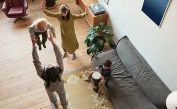 A lively indoor scene with children playing; one child is lifted in the air, while another plays a drum on the couch.
