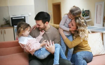 A family sits together on a couch, with two children in their laps, sharing a moment of joy and affection in a cozy home environment.