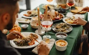 A festive dinner table set with various dishes, candles, and elegant glassware filled with drinks, inviting a warm gathering.