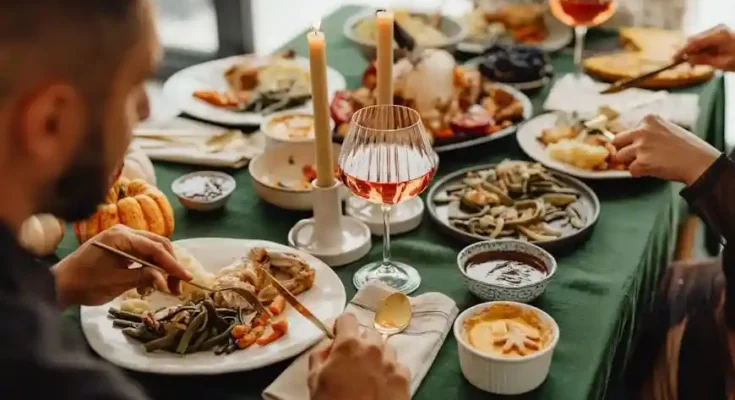 A festive dinner table set with various dishes, candles, and elegant glassware filled with drinks, inviting a warm gathering.